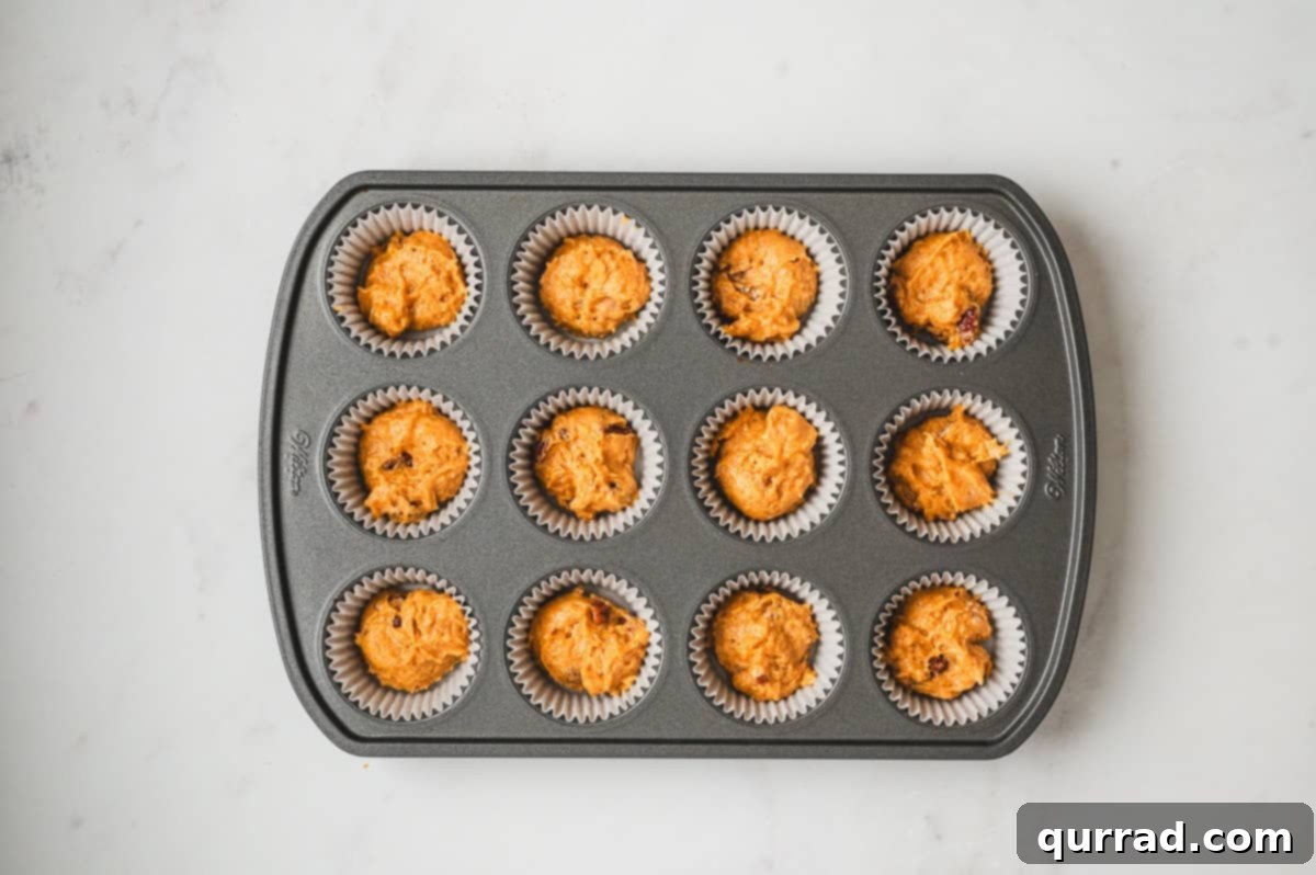 Pumpkin Cream Cheese Swirl Muffins 8 Paper liners in a muffin pan filled halfway with pumpkin muffin batter.