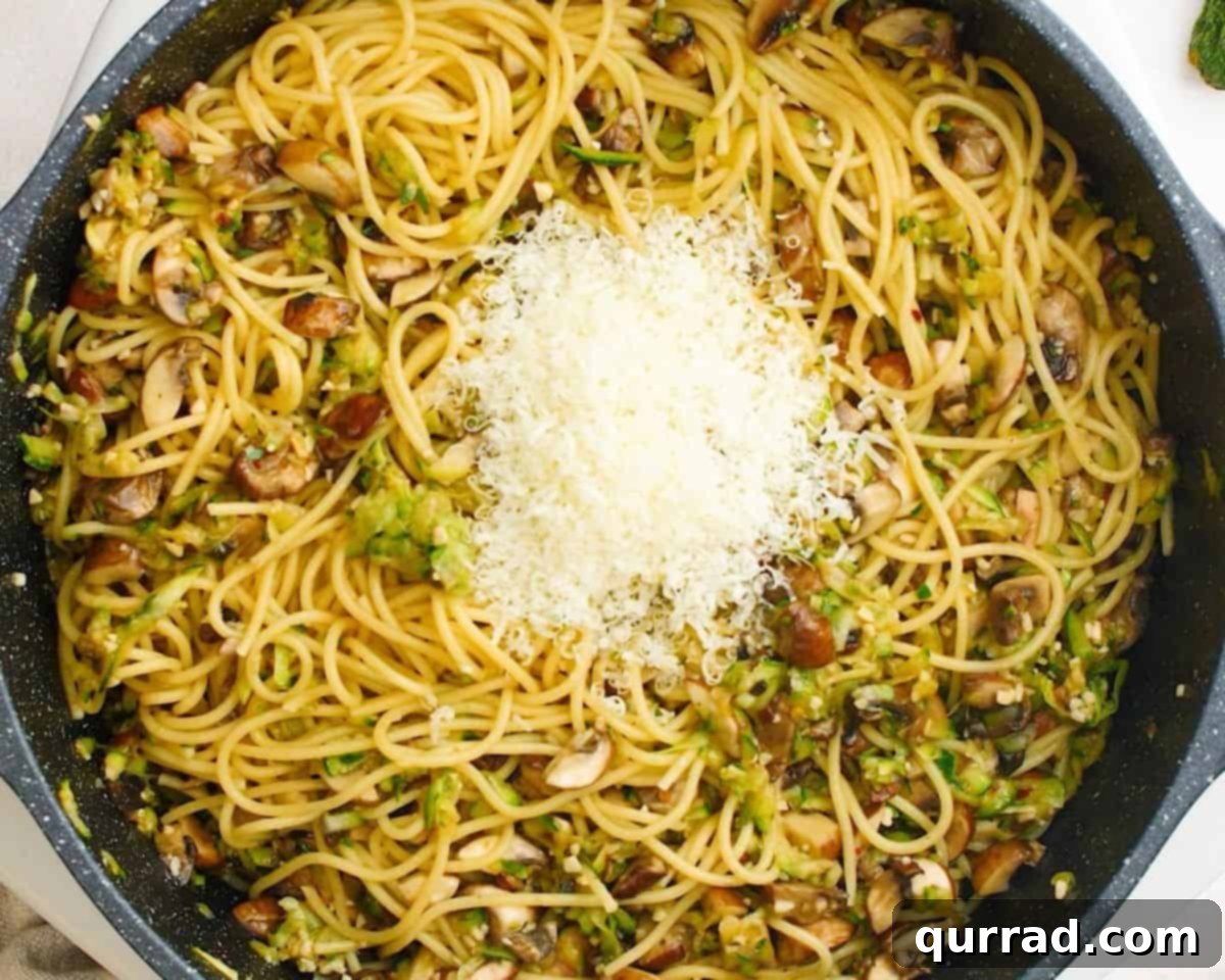 Savory Zucchini Mushroom Pasta 7 Grated Parmesan cheese being sprinkled over the tossed pasta and vegetable mixture in the pan.