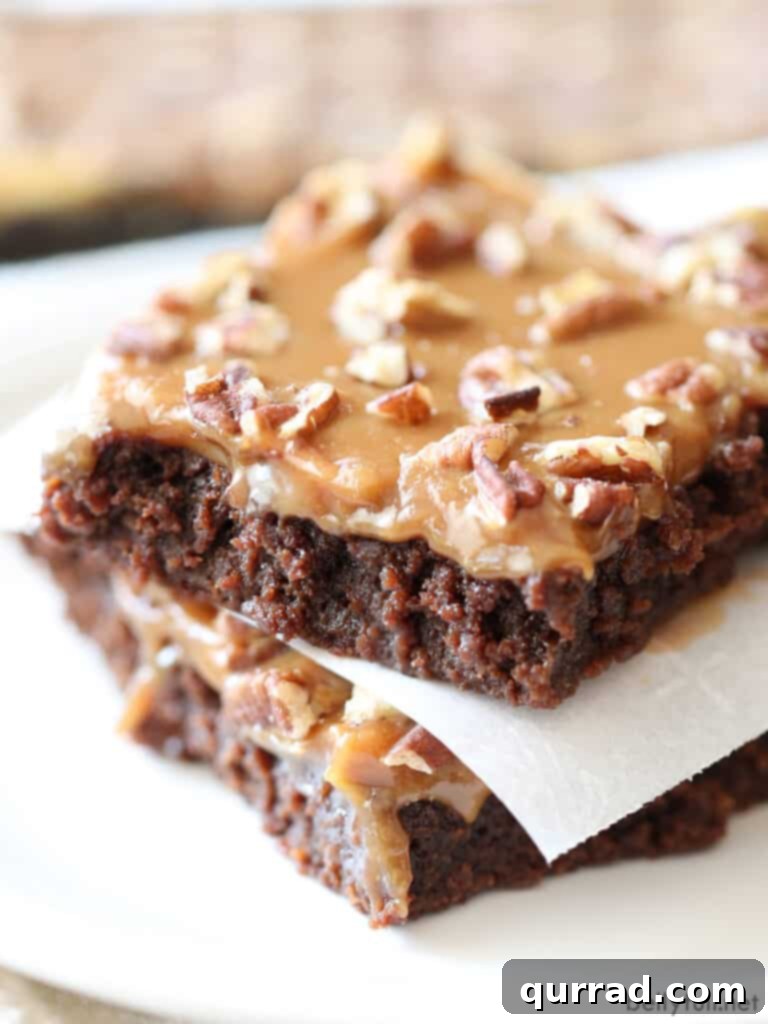 Two squares of rich, fudgy caramel pecan brownies stacked, showing off the distinct layers of chocolate brownie, golden caramel, and crunchy pecans. A perfect close-up of this ultimate dessert.