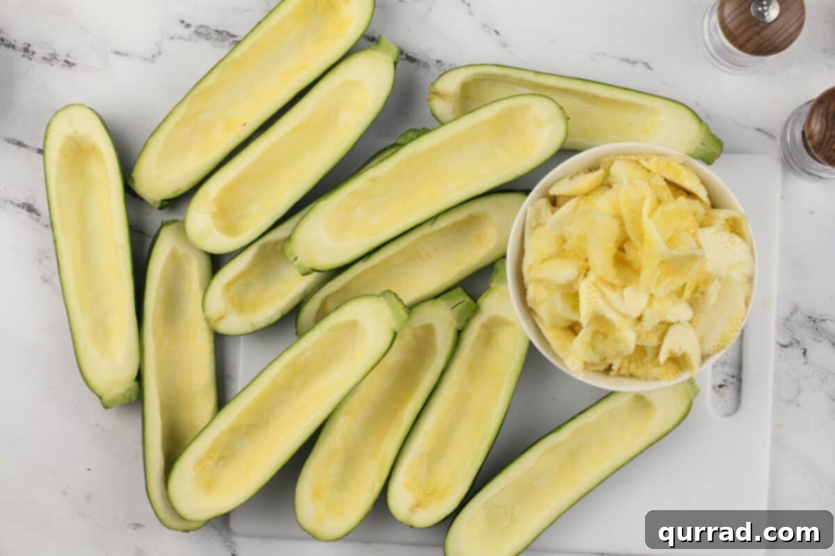 Hearty Italian Zucchini Boats 6 Hollowed out zucchini halves and a bowl of chopped zucchini flesh on a white cutting board.