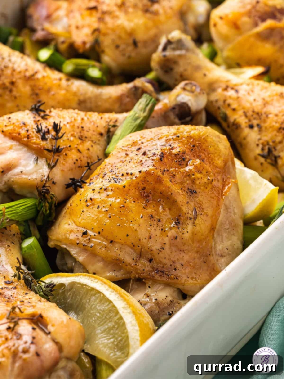 Effortless One-Pan Chicken Meal 2 Close-up of perfectly roasted, skin-on chicken thigh with a golden-brown, crispy skin, resting among tender vegetables and lemon slices in a roasting pan.