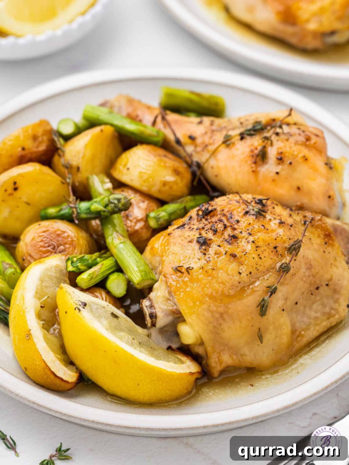 Effortless One-Pan Chicken Meal 5 Plated roasted chicken thighs with lemon wedges, surrounded by roasted potatoes and asparagus, ready to be served.