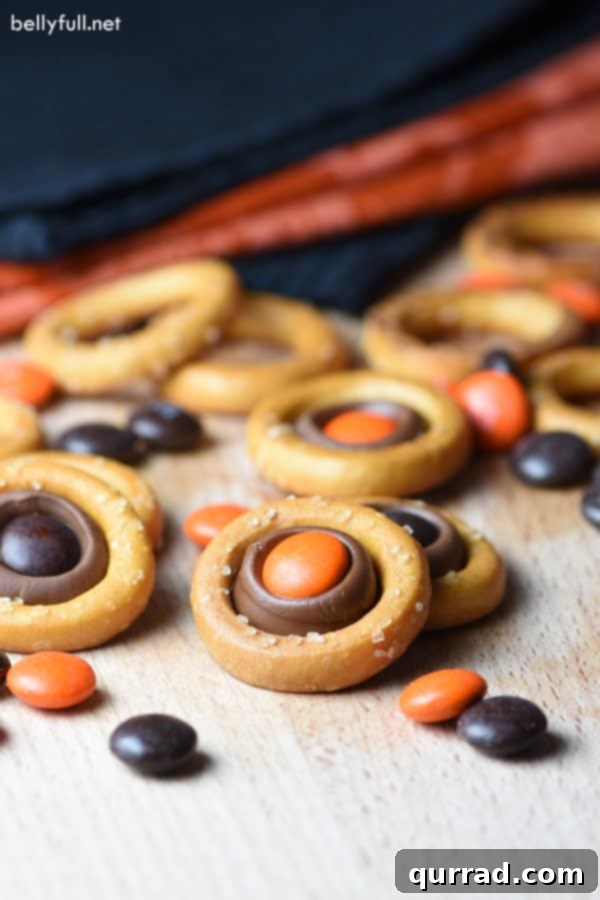 Easy Halloween Pretzel Rings: Sweet & Salty Treat Three Halloween Pretzel Rings artfully arranged, showcasing their vibrant orange and brown M&Ms and gooey chocolate centers against a dark, spooky background