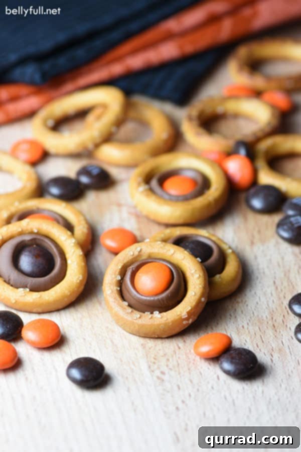 Easy Halloween Pretzel Rings: Quick Halloween Snack A stack of Halloween Pretzel Rings, glistening with melted Hershey's chocolate and topped with orange and brown M&Ms, ready to be enjoyed as a spooky snack