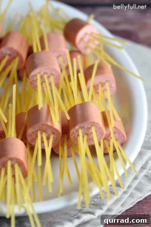 Spaghetti-Pierced Hot Dog Bites 3 Close-up of cooked Threaded Spaghetti Hot Dog Bites in a bowl, coated with butter and Parmesan. The spaghetti strands protrude from the hot dog pieces.