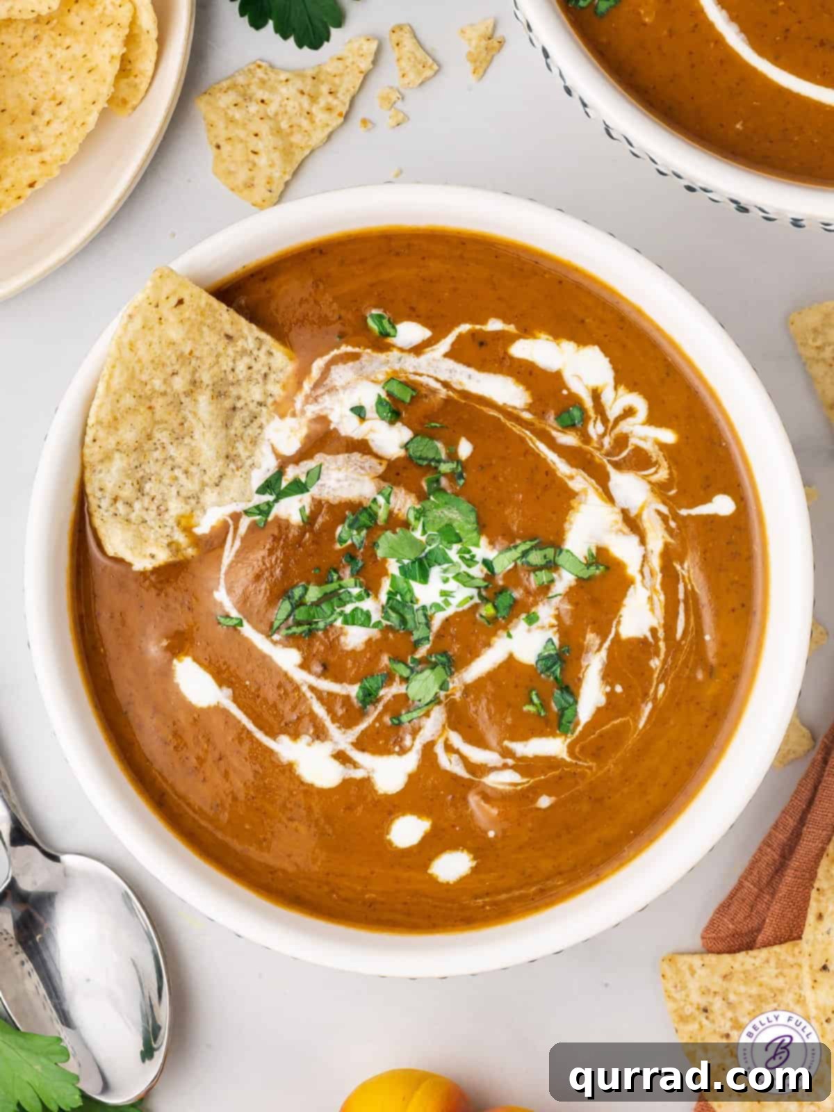 Golden Harvest Pumpkin Black Bean Delight 2 Overhead view of a bowl of creamy pumpkin black bean soup, garnished with a swirl of heavy cream and a crunchy tortilla chip.