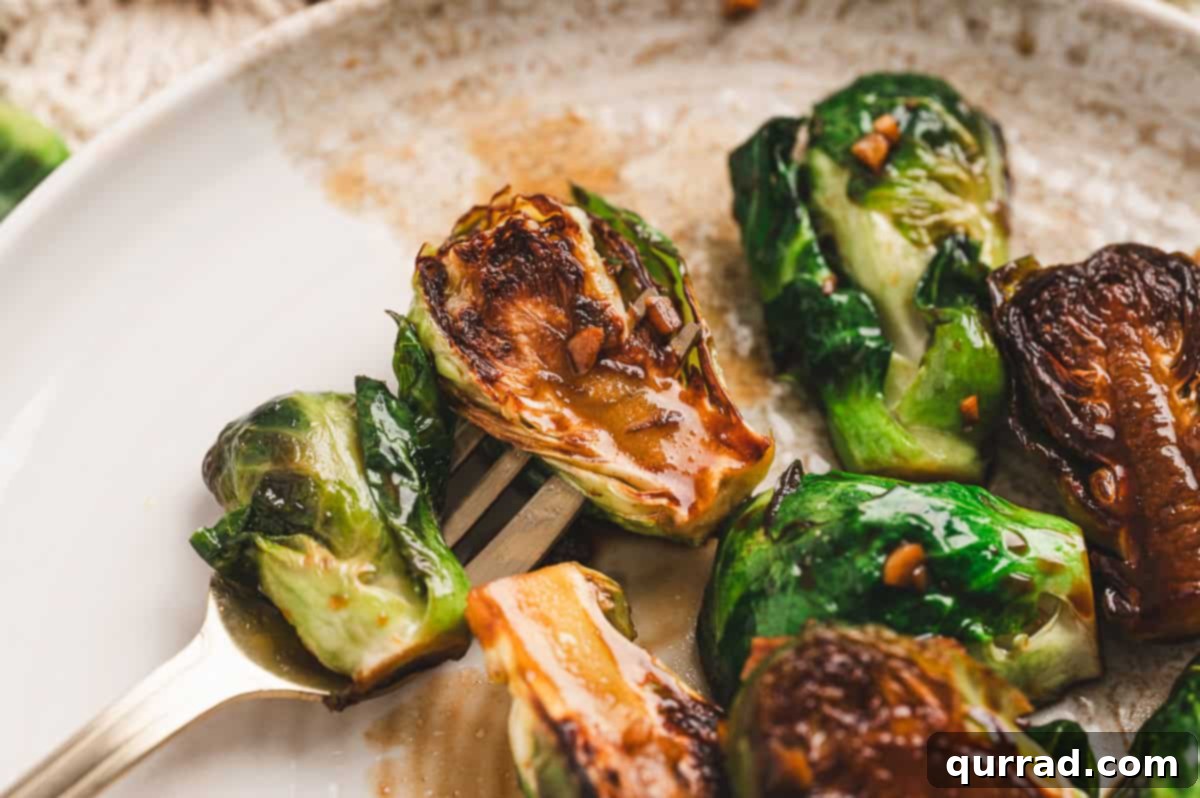 Caramelized Molasses Brussels Sprouts 10 Fork holding a halved Brussels sprout with caramelized edges and glossy molasses glaze on a white plate.