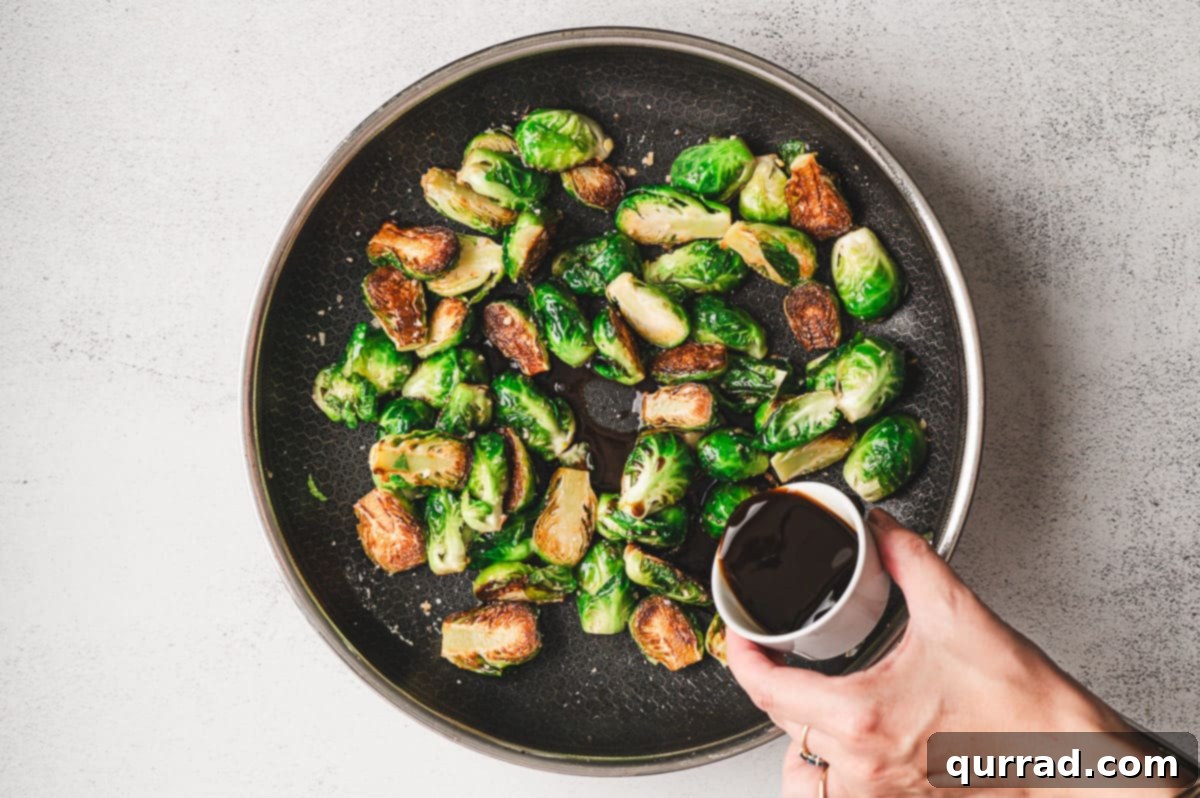 Caramelized Molasses Brussels Sprouts 7 Hand pouring a small bowl of molasses mixture into a skillet filled with sautéed Brussels sprouts.