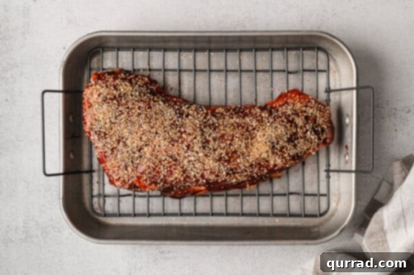 Uncooked tri tip with layer of sauce and dried garlic on roasting rack, ready for the oven