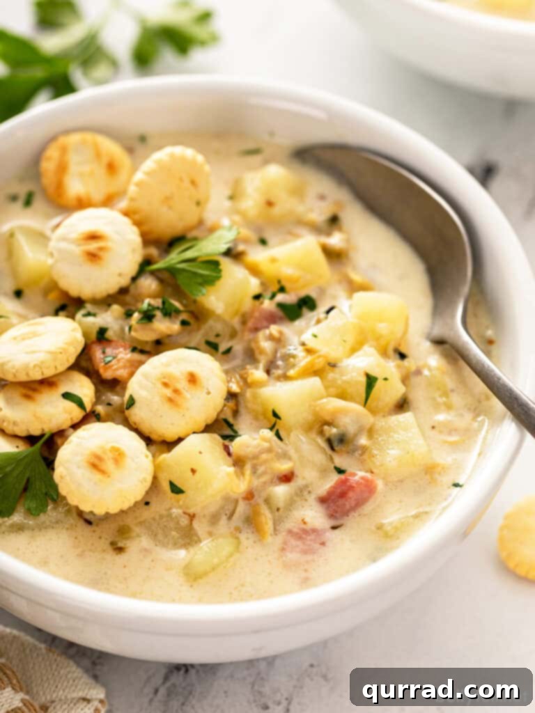A beautiful bowl of thick and creamy New England Clam Chowder, garnished with fresh parsley and a side of oyster crackers, ready to be enjoyed.