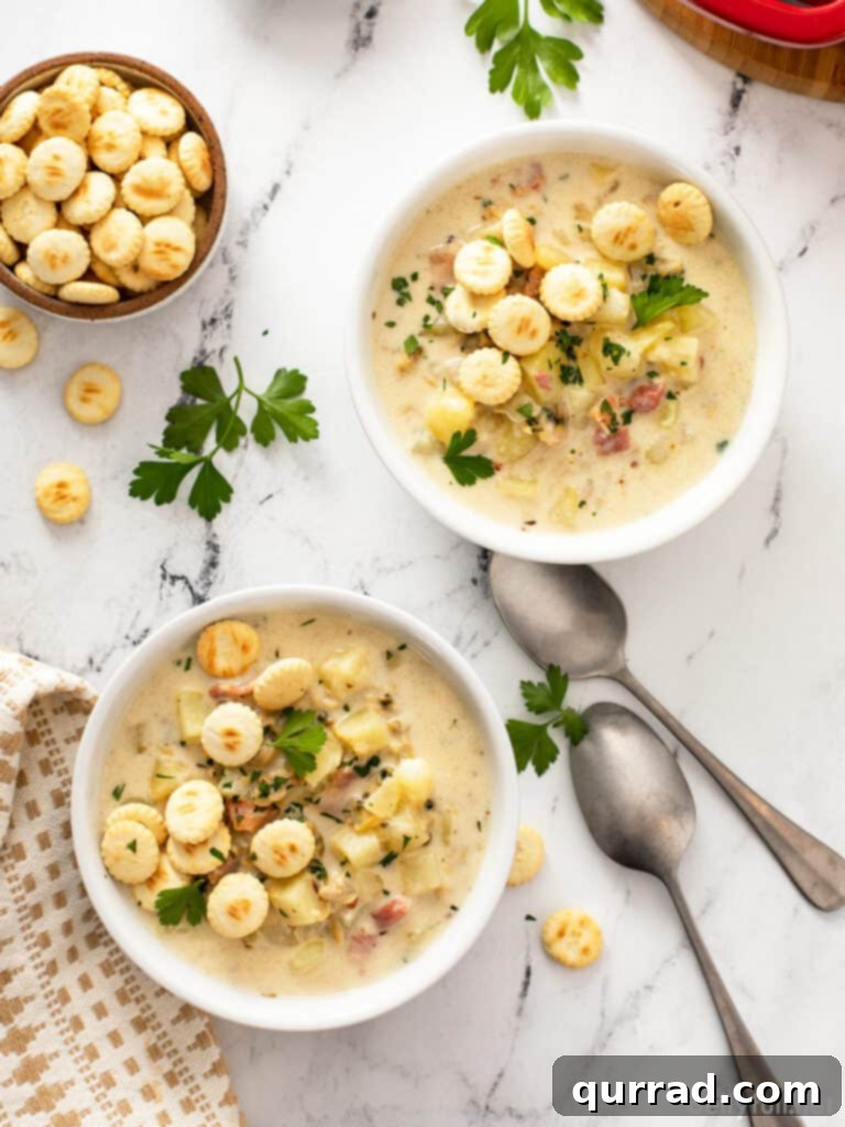 Two bowls of creamy New England Clam Chowder, generously topped with crispy oyster crackers and fresh parsley, presented on a rustic wooden table.