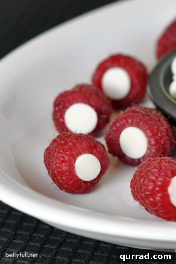 A close-up shot of several fresh raspberries expertly stuffed with rich dark chocolate, showcasing the glossy texture of the chocolate against the deep red of the berries, presented on a minimalist white plate.