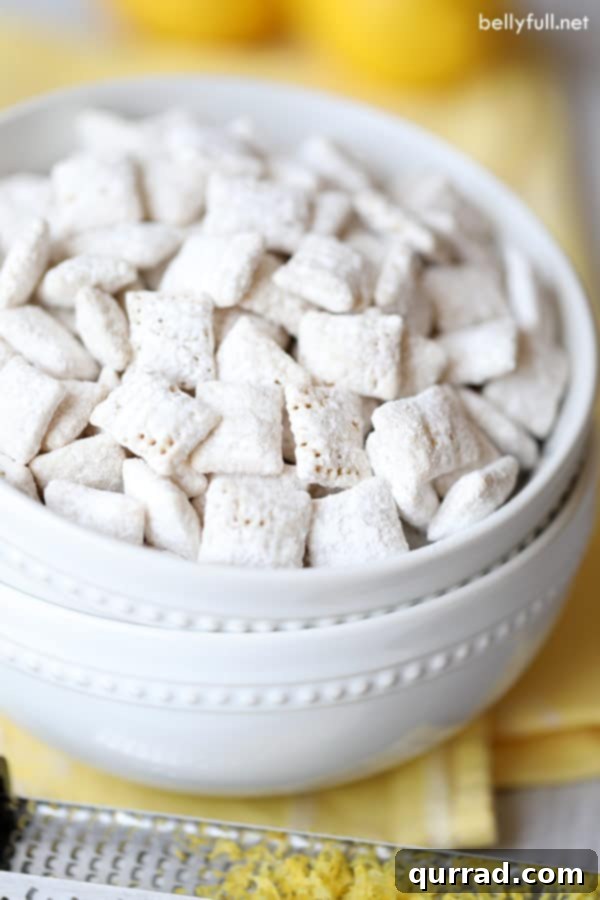 15-minute Lemon Muddy Buddies with Rice Chex cereal, white chocolate, lemon juice, and lemon zest. Try not to eat all of it in one sitting! #muddybuddies #puppychow #lemonmuddybuddies #lemonpuppychow #lemondesserts close up of Lemon Muddy Buddies in a white bowl, showing the powdered sugar coating and flecks of lemon zest