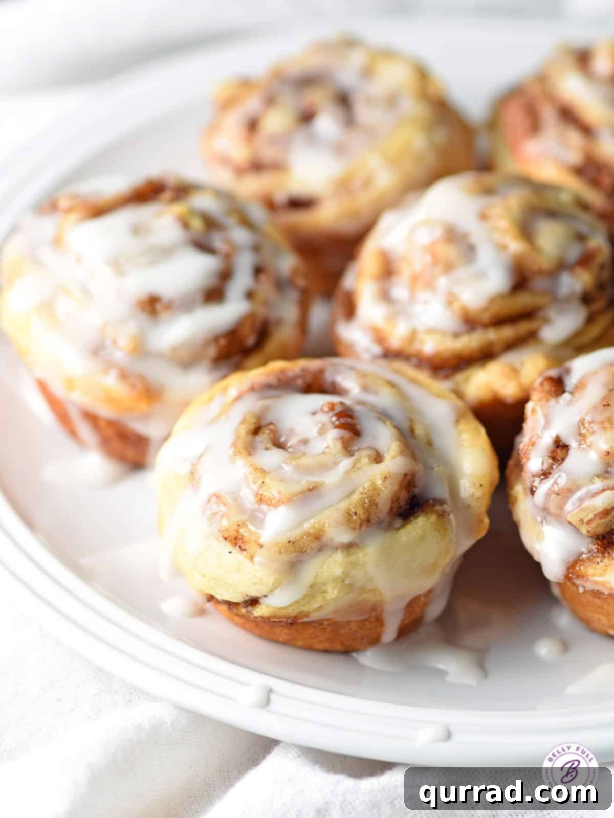Effortless Mini Cinnamon Buns 8 Mini cinnamon rolls generously drizzled with white icing on a white plate, ready to be eaten.