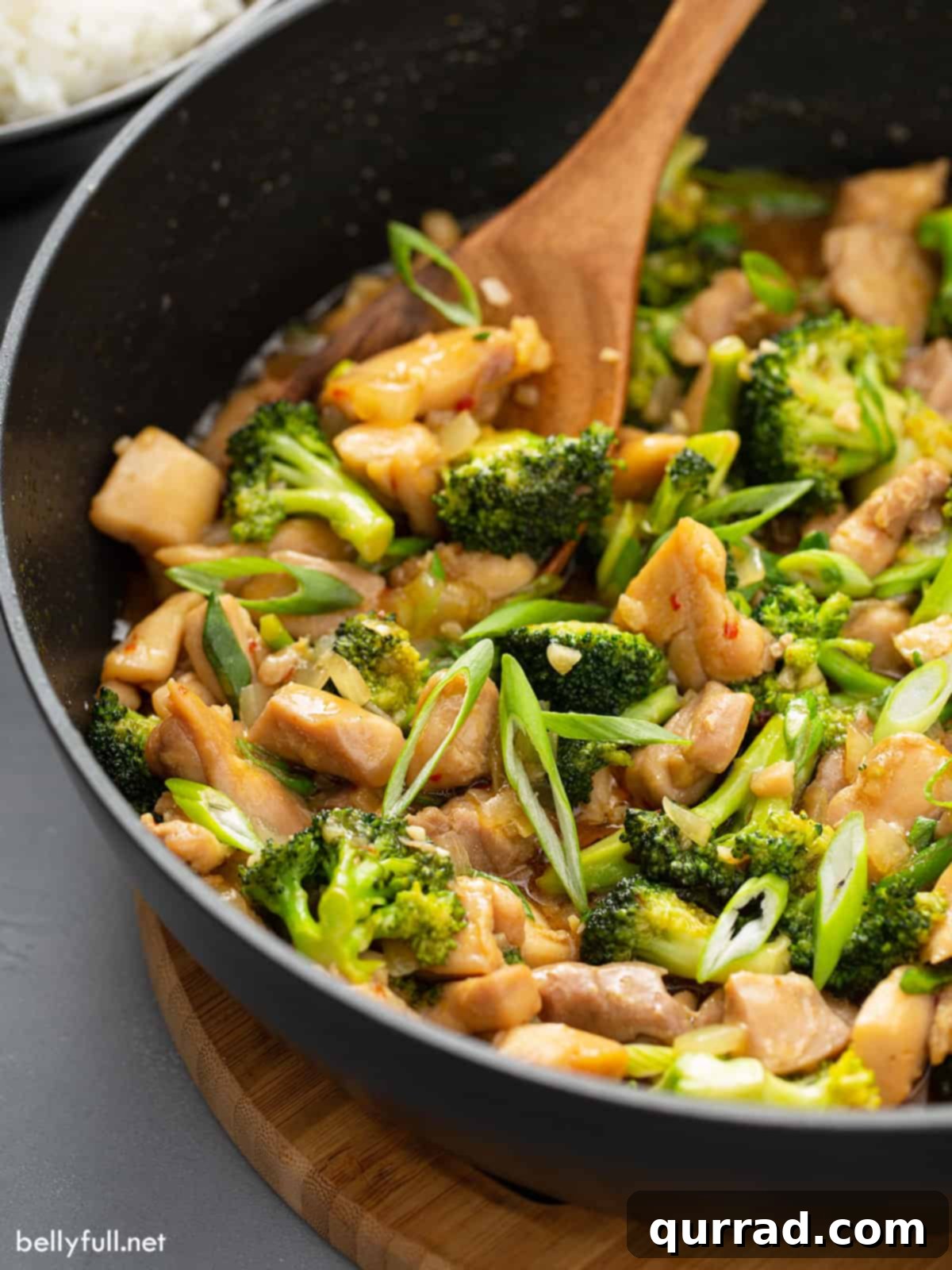 Savory Chicken and Broccoli Stir Fry 10 Chicken stir fry in a skillet with a wooden spoon, showcasing rich sauce and tender ingredients.