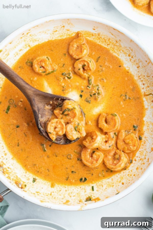 Creamy Thai Coconut Shrimp Curry 3 A white bowl filled with creamy Thai Shrimp Curry, garnished with fresh herbs and a wooden spoon resting inside.