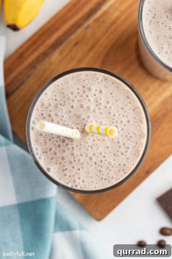 Morning Buzz Banana Blend 3 Overhead view of a delicious breakfast banana smoothie in a glass with two yellow striped straws, ready to be enjoyed.