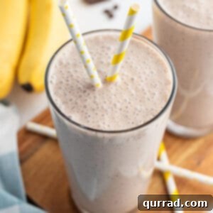 banana smoothie in tall glass with yellow and white striped straw and bananas in the background