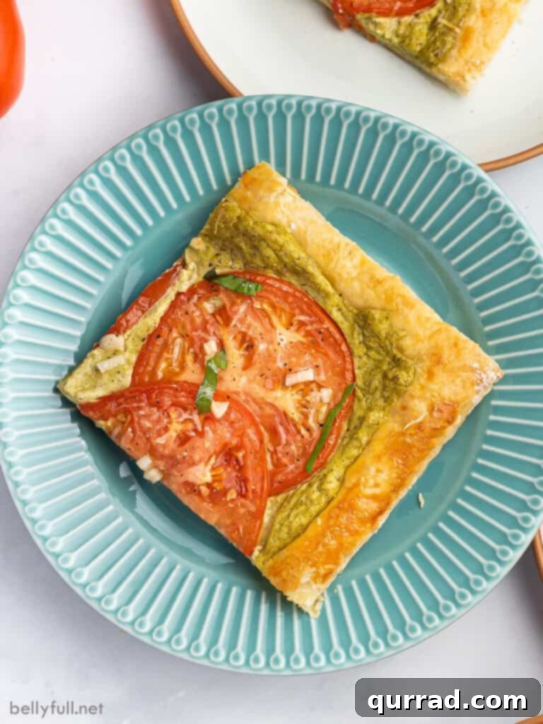 A blue plate featuring a single square slice of a tomato puff pastry tart, highlighting its intricate layers and vibrant toppings.