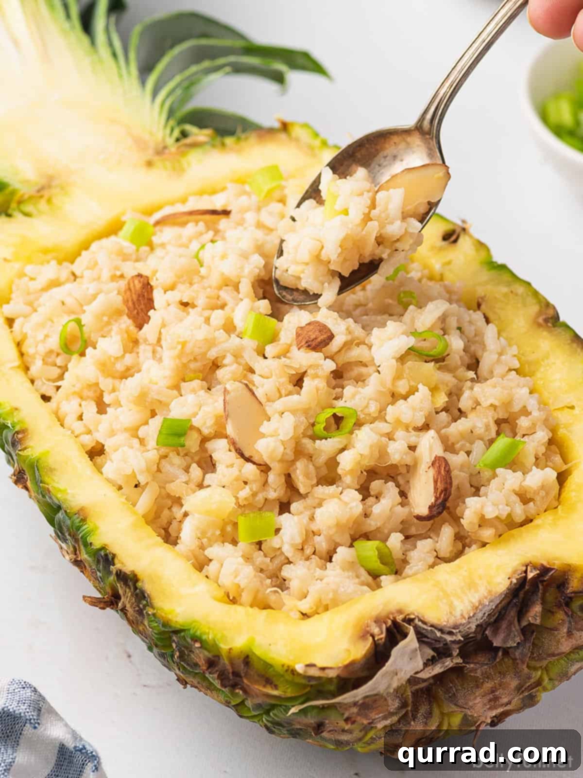 Tropical Coconut Pineapple Rice 5 A close-up shot of creamy coconut rice with pineapple pieces, garnished with scallions, served in a hollowed pineapple half.