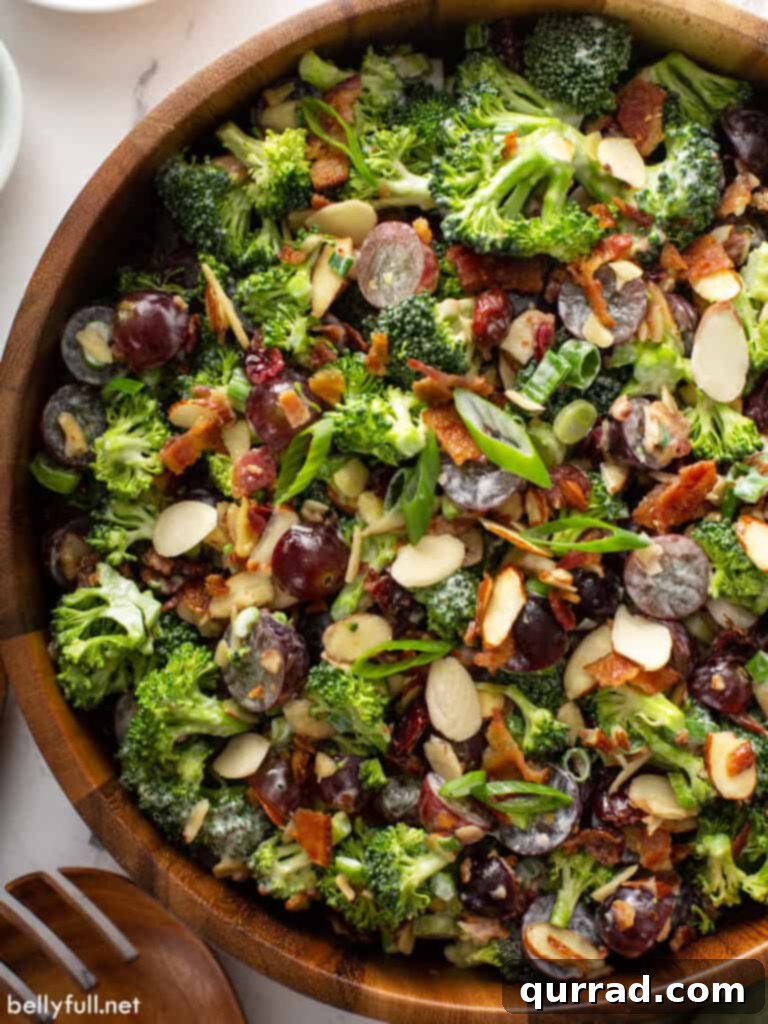 Sweet & Tangy Broccoli Crunch 2 Overhead close-up of a vibrant broccoli salad in a rustic wooden serving bowl, showcasing the fresh ingredients like green broccoli, red grapes, and bacon bits.
