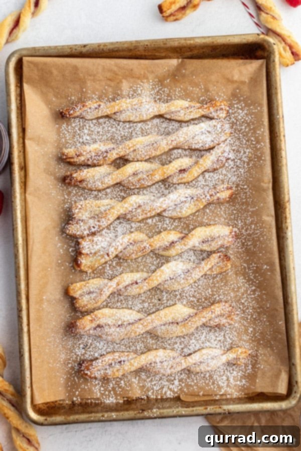 Golden Flaky Jam Spirals 3 An overhead shot showcasing rows of uncooked jam puff pastry twists meticulously arranged on brown parchment paper, awaiting their turn in the oven.