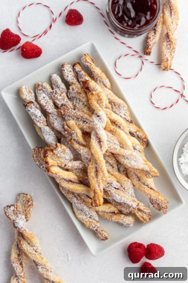 Golden Flaky Jam Spirals 4 An overhead view of freshly baked jam puff pastry twists, generously dusted with powdered sugar, presented on an elegant white serving tray.