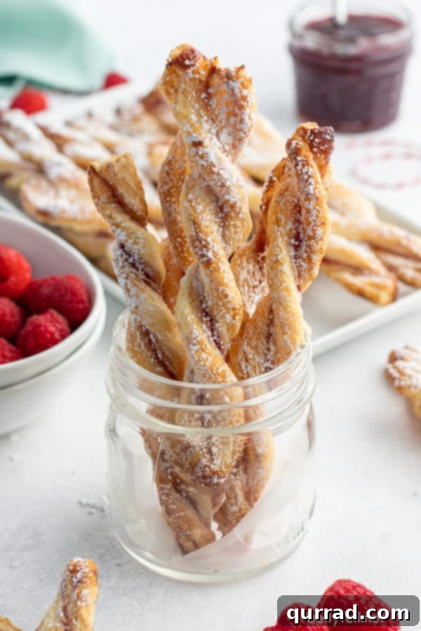 Golden Flaky Jam Spirals 5 Elegantly arranged jam puff pastry straws standing upright in a clear glass jar, ready for serving or display, highlighting their charming presentation.