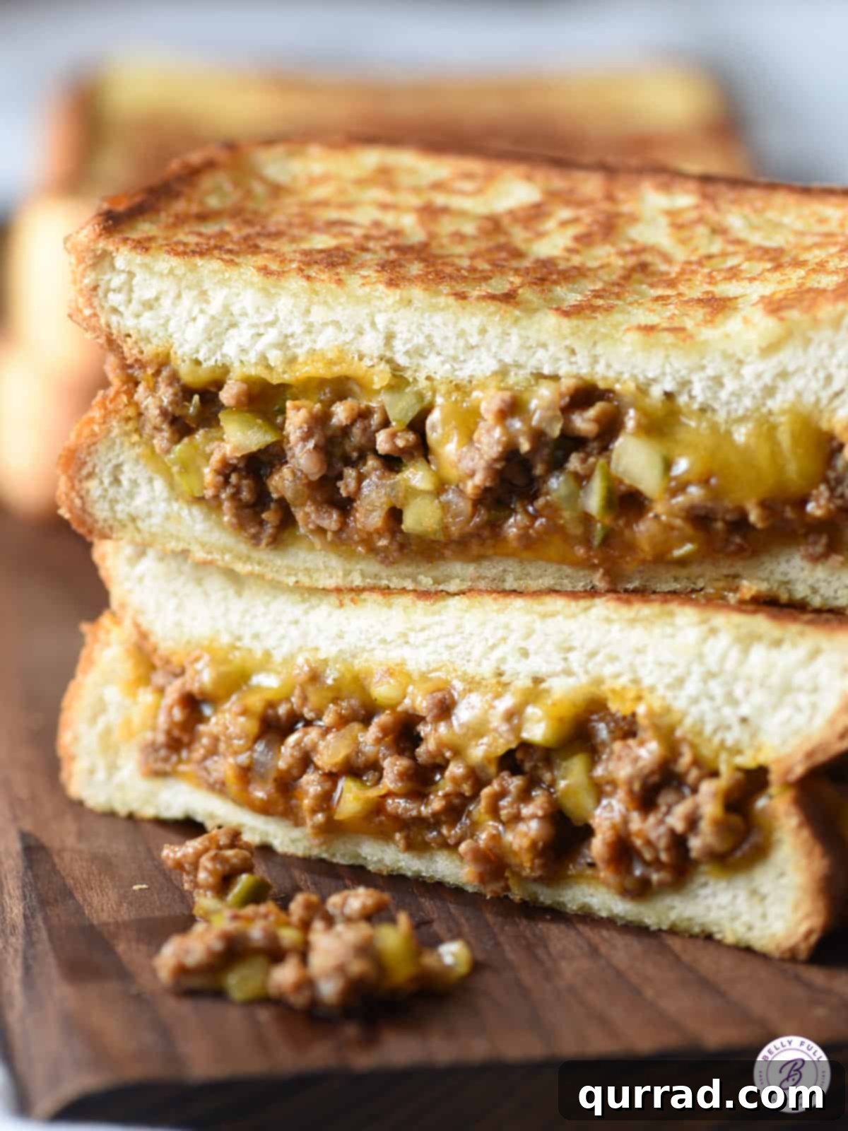 Tangy Dill Pickle Sloppy Joe Melt 2 Two halves of a Dill Pickle Sloppy Joe Grilled Cheese sandwich stacked, showcasing the crispy bread, melted cheese, and savory sloppy joe filling with diced pickles.