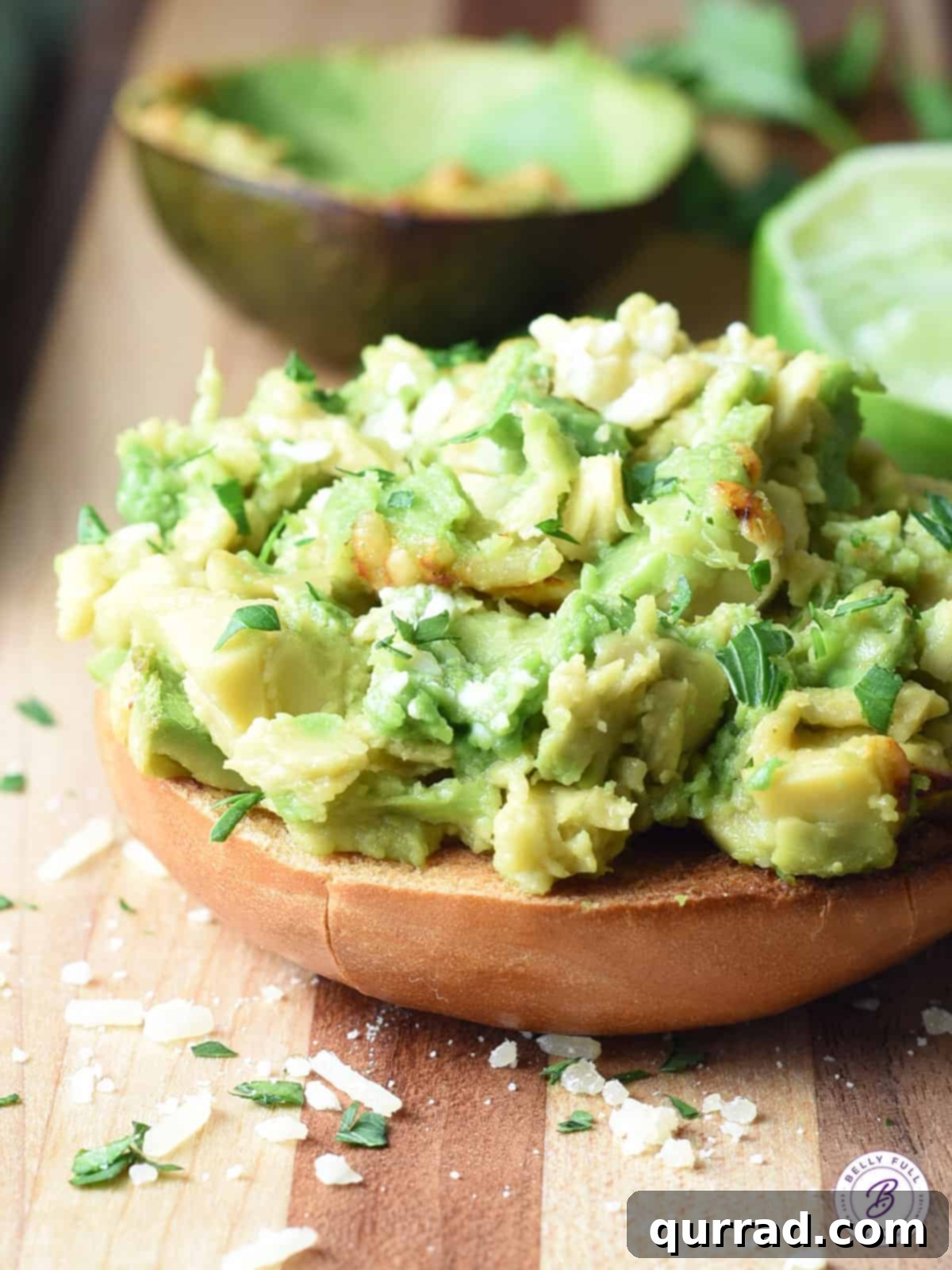 Golden Broiled Parmesan-Lime Avocado 4 A half of broiled avocado with melted Parmesan and lime on a toasted bagel, garnished with fresh parsley, demonstrating a serving suggestion.