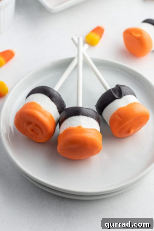 Three Halloween Marshmallow Pops with orange and black candy melts, artfully arranged on a clean white plate, ready for a festive gathering.