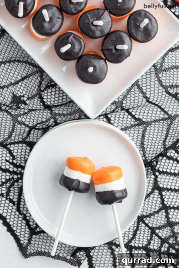 An overhead view capturing two delightful Halloween Marshmallow Pops resting on a clean white plate, which is set against a black spiderweb tablecloth, perfectly capturing the spooky festive mood.