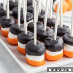 White tray displaying several black and orange candy coated marshmallows on sticks, ready for a Halloween celebration.