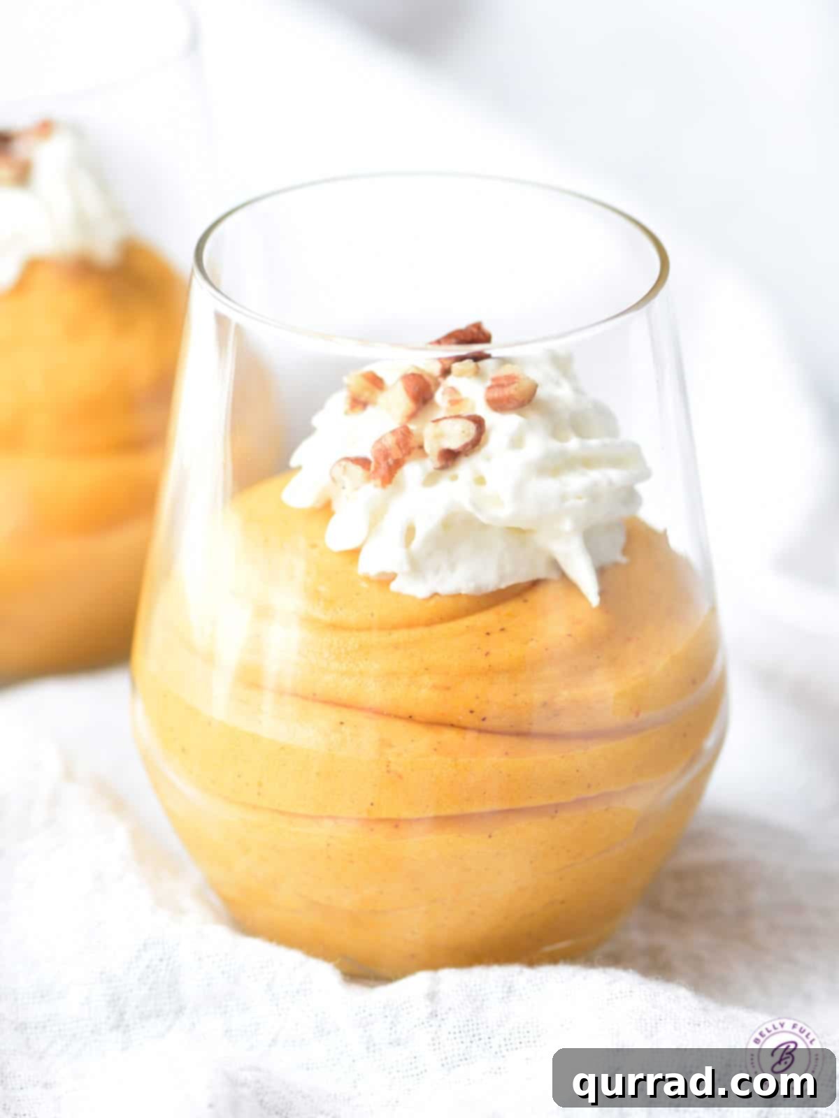 This Pumpkin Fluff is a super simple, light, and creamy dessert made for pumpkin lovers. Perfect for Fall, Thanksgiving, or all year round! #pumpkinrecipes #pumpkinrecipeseasy #pumpkinrecipesdessert #pumpkinfluff Pumpkin fluff mousse in a parfait glass, topped with a swirl of whipped cream and chopped pecans.