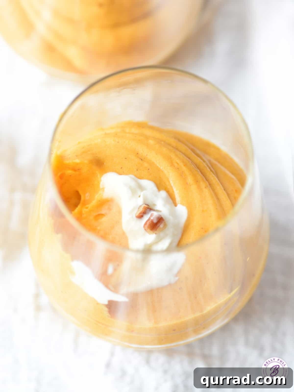 This Pumpkin Fluff is a super simple, light, and creamy dessert made for pumpkin lovers. Perfect for Fall, Thanksgiving, or all year round! #pumpkinrecipes #pumpkinrecipeseasy #pumpkinrecipesdessert #pumpkinfluff An overhead shot of pumpkin mousse beautifully presented in a parfait glass.