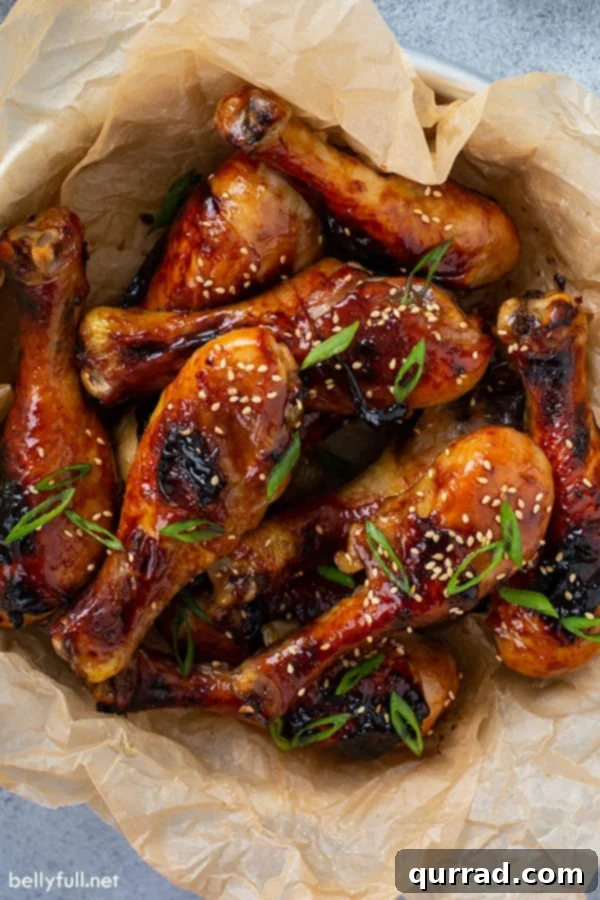 Overhead picture of honey soy chicken drumsticks in a bowl, garnished with green onions and sesame seeds.