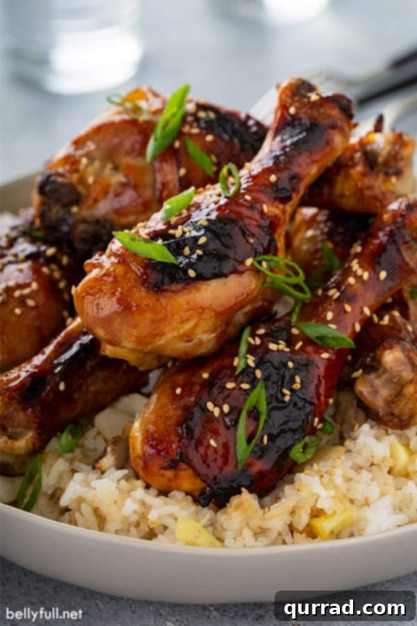 Honey soy chicken drumsticks stacked on top of a bed of Pineapple Coconut Rice in a white bowl.