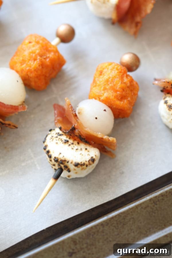 Irresistible Sweet Potato Casserole Bites with Candied Bacon and Toasted Marshmallow Sweet potato casserole bites on toothpicks, featuring sweet potato tots, pearl onions, candied bacon, and charred marshmallows, presented on a rustic wooden board.