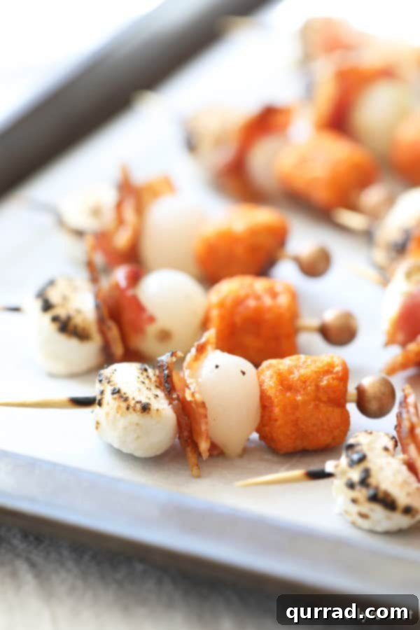 Individual Sweet Potato Casserole Bite – A Festive Appetizer Close-up of a single Sweet Potato Casserole Bite on a toothpick, highlighting the layers of sweet potato tot, pearl onion, glistening candied bacon, and perfectly torched marshmallow.