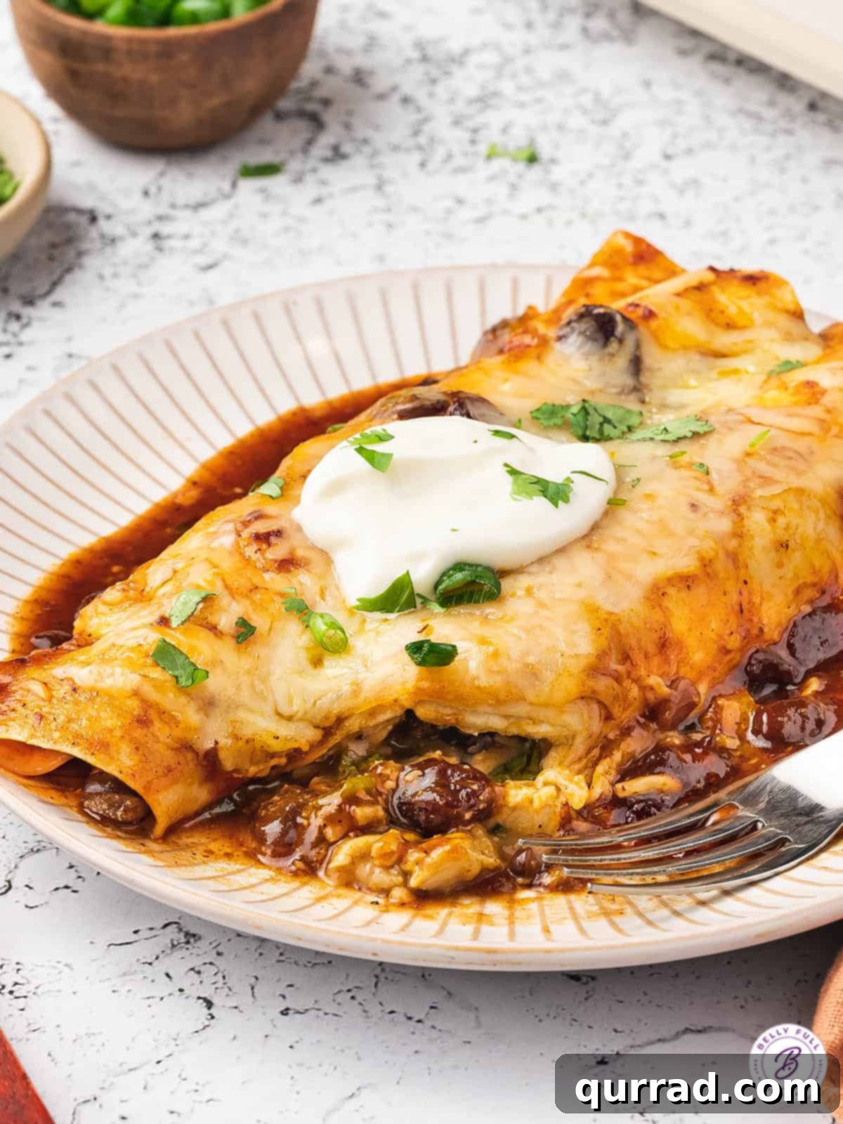 Close-up of two cranberry turkey enchiladas on a plate, garnished with a dollop of sour cream.