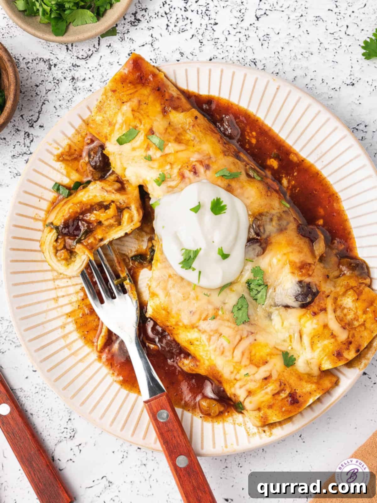 Overhead shot of two finished cranberry turkey enchiladas on a plate with a fork, ready to be eaten.
