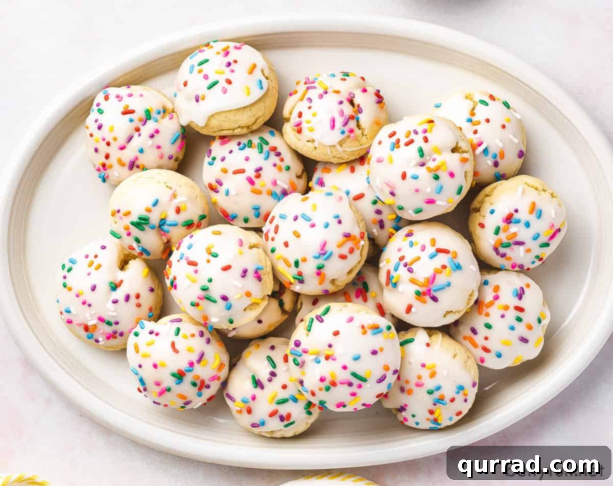 Sweet Italian Delights 4 A large white plate generously filled with Italian Cookies, each perfectly round, iced in white, and adorned with festive rainbow sprinkles, creating a vibrant display.