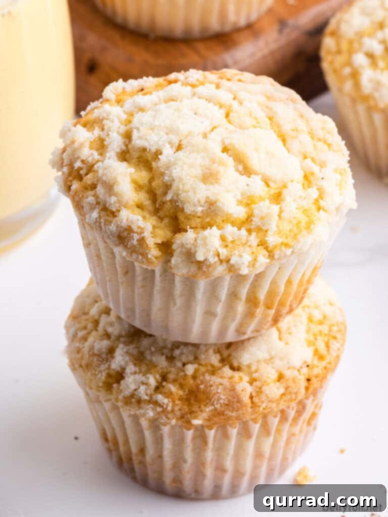 Spiced Eggnog Muffins 2 Two fluffy Eggnog Muffins with golden streusel topping, stacked elegantly on a festive background, hinting at their rich, cake-like texture perfect for holiday enjoyment.