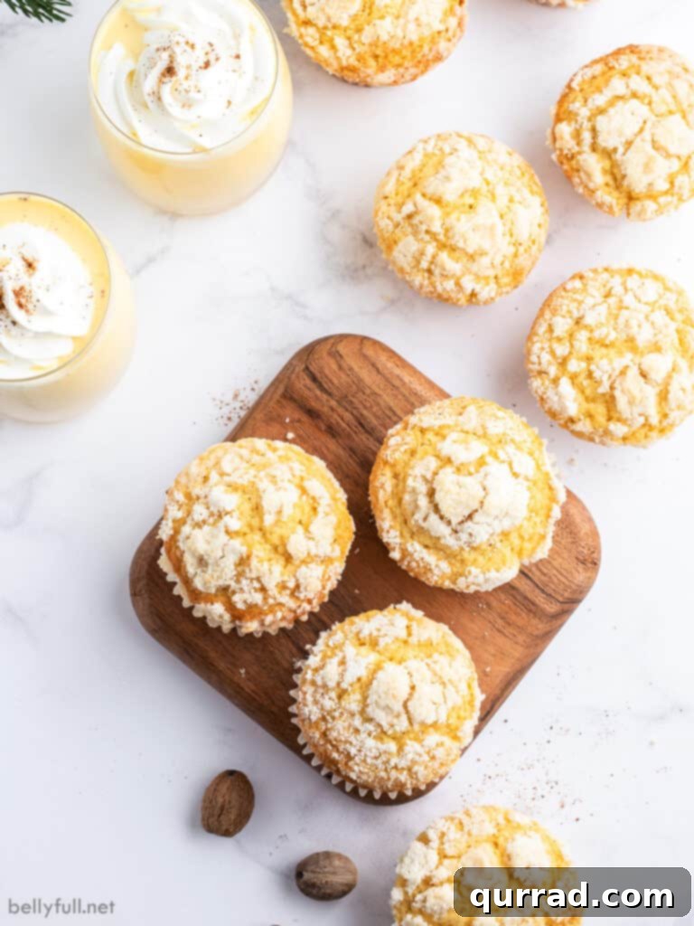 Spiced Eggnog Muffins 4 An overhead view of eight freshly baked Eggnog Muffins with streusel topping, arranged around two glasses of creamy eggnog, showcasing their delightful appearance.