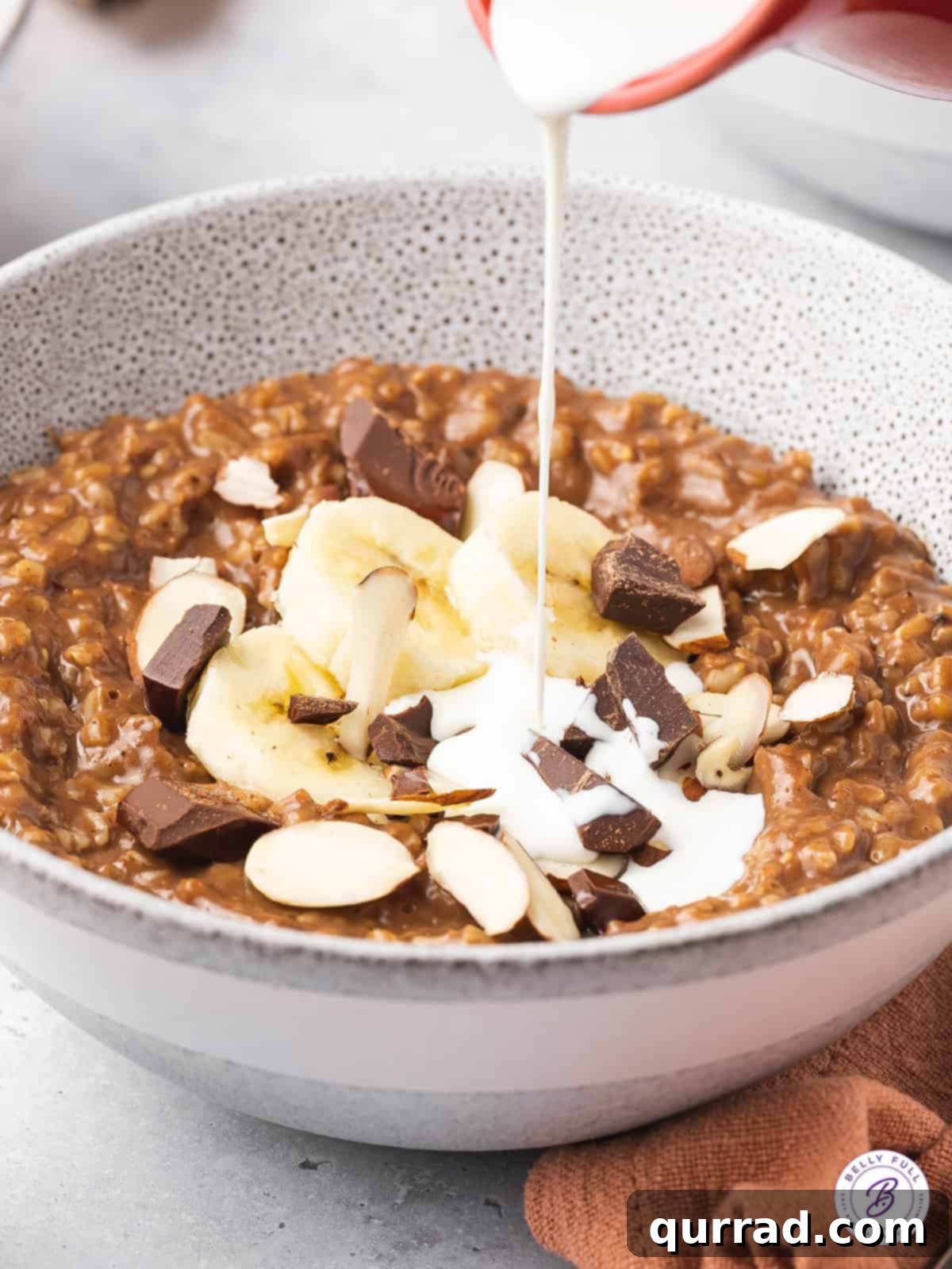 Cocoa-Almond Steel Cut Oatmeal Heavy cream being drizzled into a bowl of chocolate steel cut oatmeal, ready for toppings.
