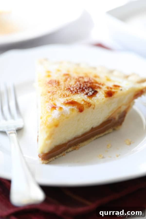Torched Caramel Custard Pie 2 A perfectly sliced Caramel Creme Brulee Pie, showcasing its distinct layers of golden-brown caramelized sugar, creamy custard, and dark caramel, all nestled in a golden pie crust.