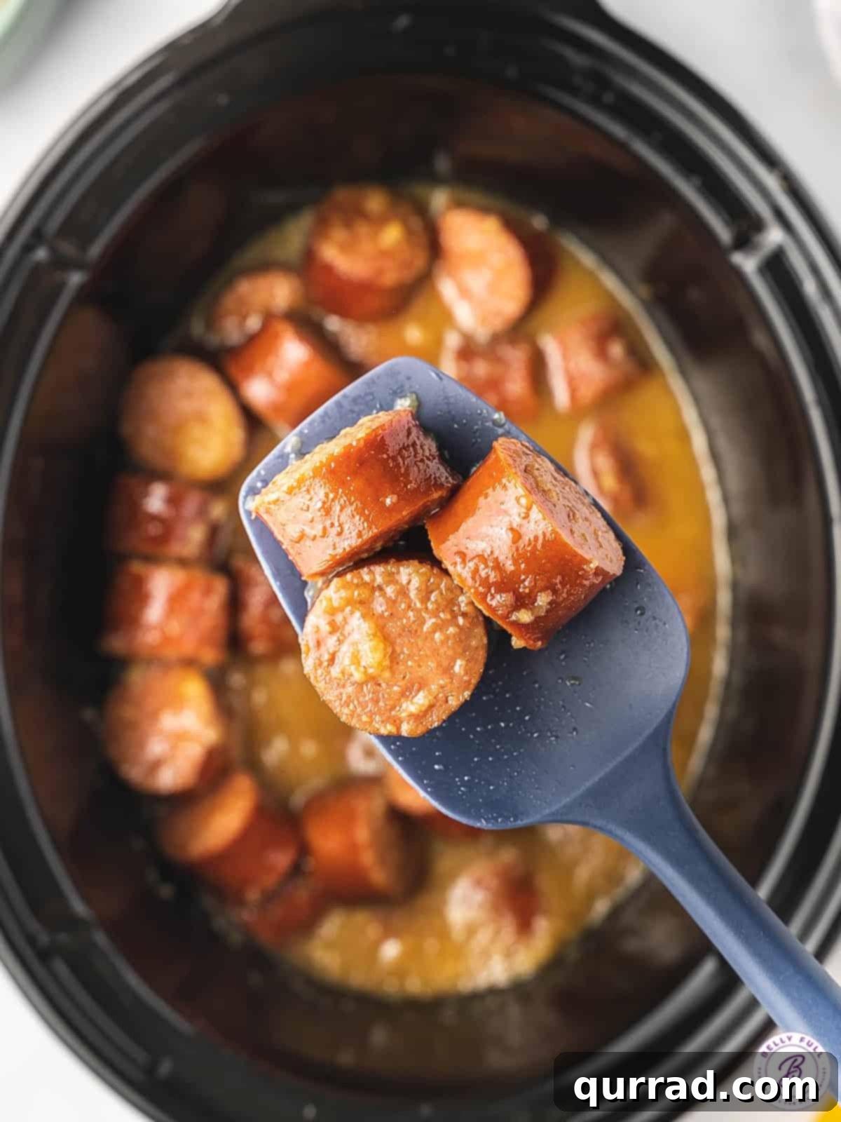 Slow Cooker Apple Kielbasa Poppers 4 3 pieces of cooked kielbasa on spoon over a crock pot