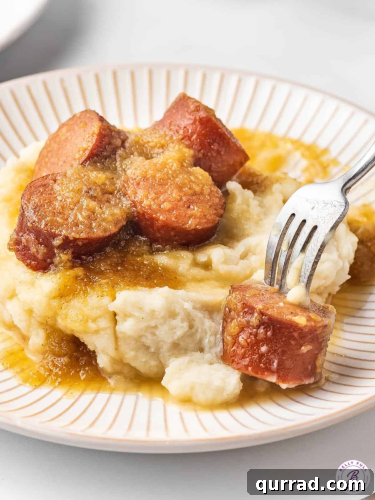Slow Cooker Apple Kielbasa Poppers 5 pieces of smoked sausage on fork over mashed potatoes