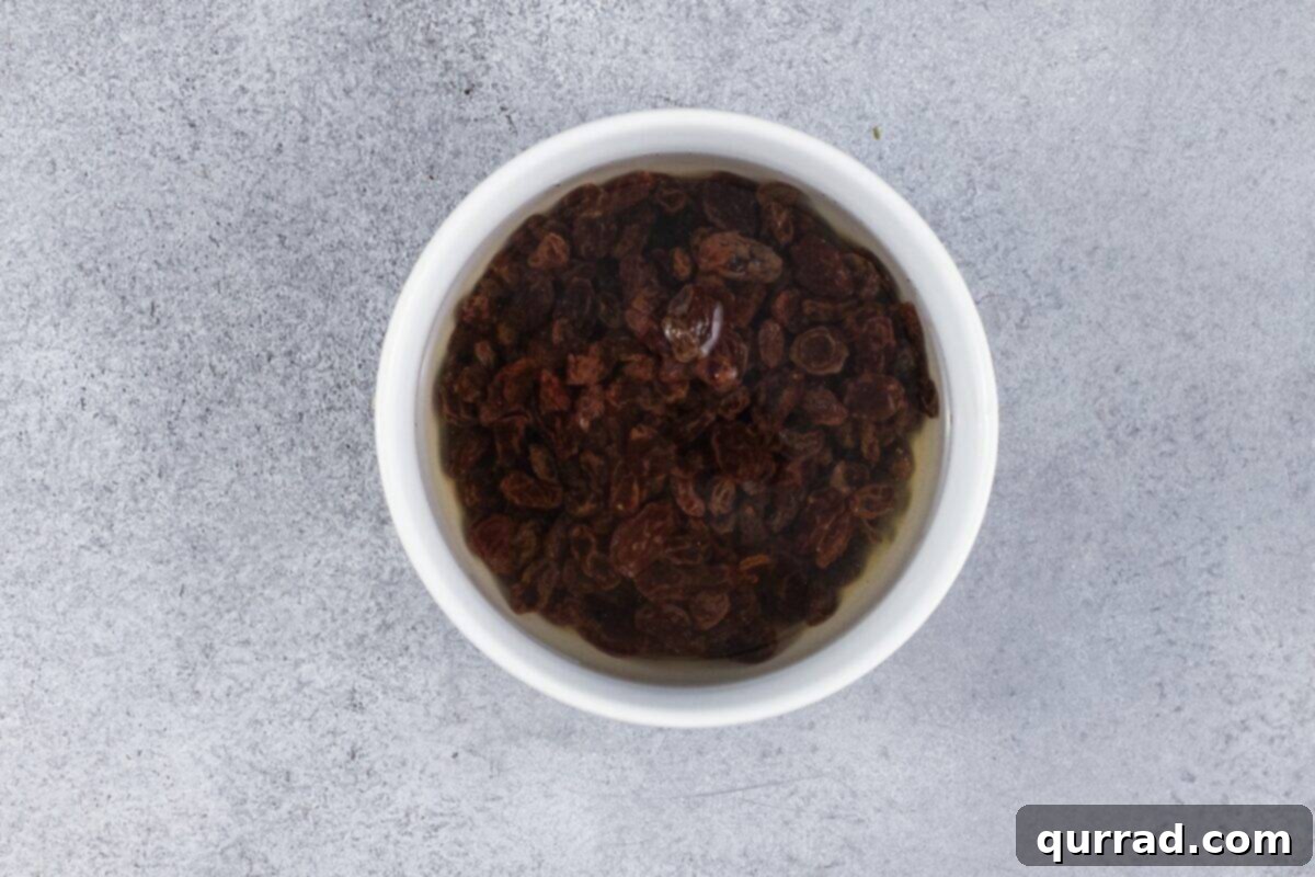 Golden Baked Noodle Pudding 5 Raisins soaking in a white bowl.