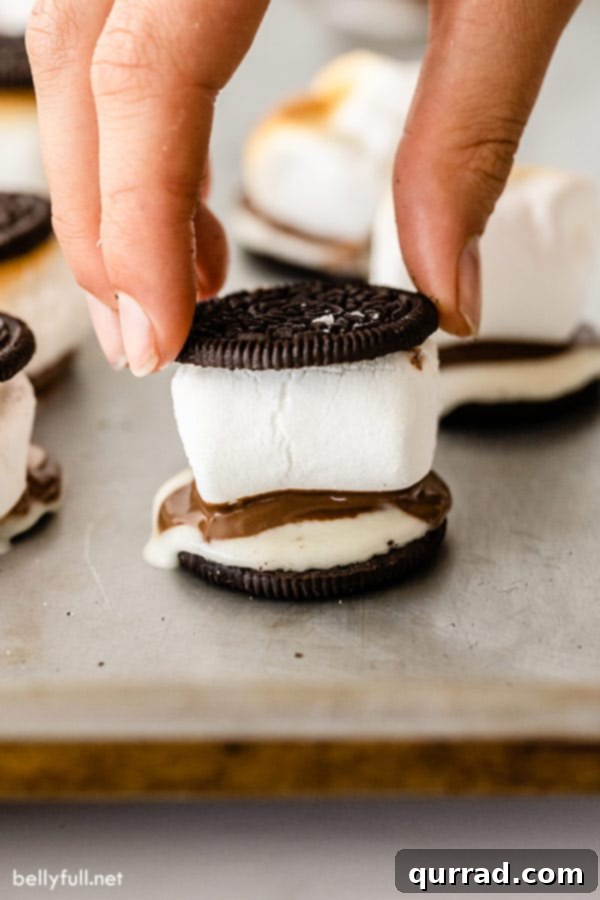Oreo Smores 3 A hand carefully places an Oreo cookie top onto a freshly broiled marshmallow and chocolate on an Oreo base